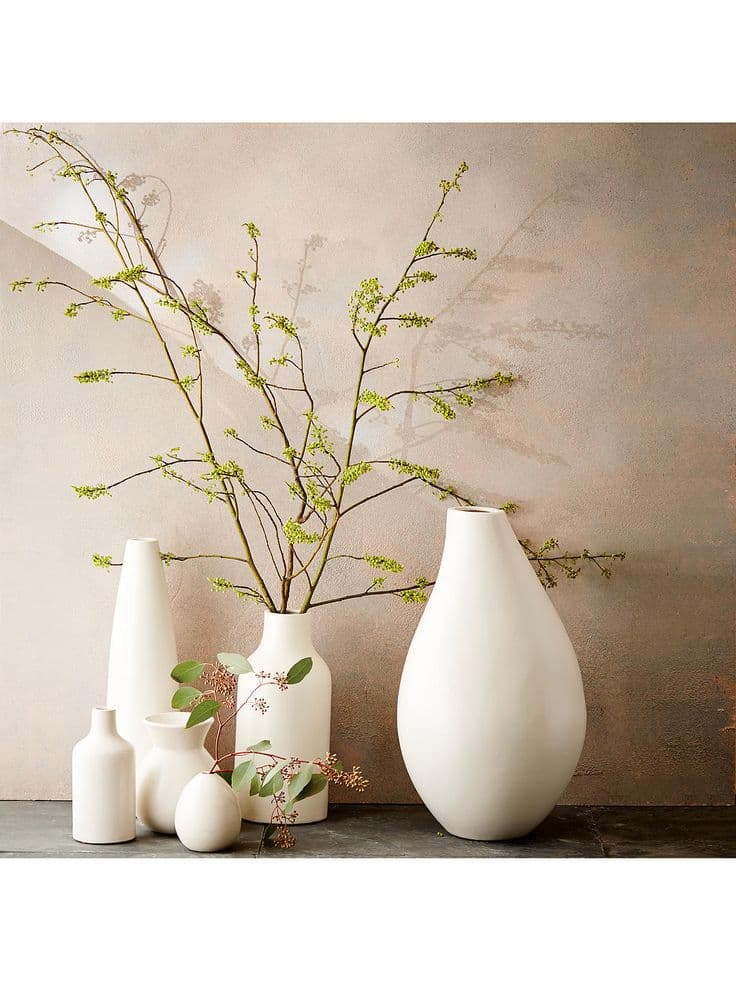 three white vases with flowers in them sitting on a gray table next to ...